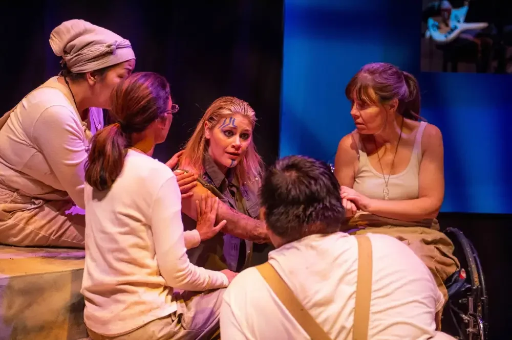 A scene from our production "Anitgone" featuring Sarah Luby and Debbie Patterson sitting in a circle with three other actors. They are all reaching out to touch Sarah's arm, dressed in white and beige costumes