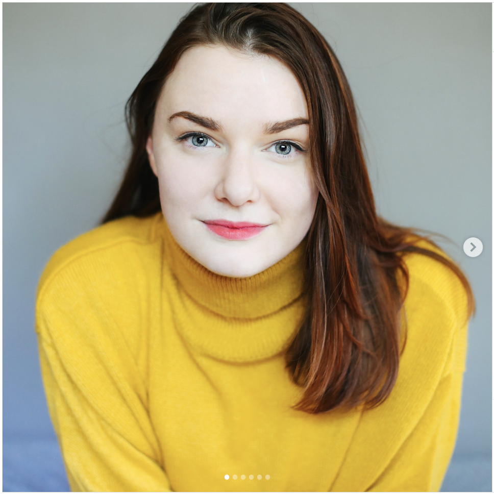 Photo of Emily King. She has light skin, blue eyes, long brown hair, and is smiling softly while looking at the camera