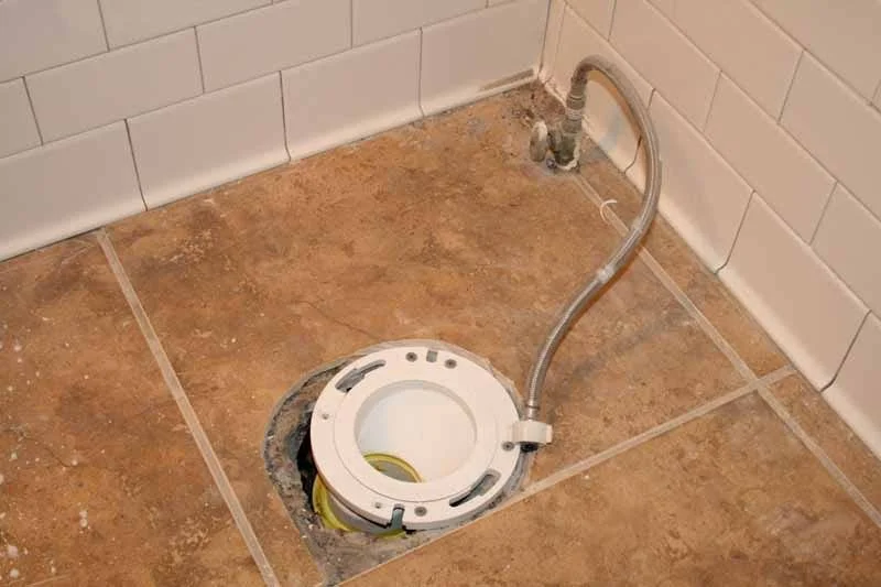 Toilet bowl removed, exposing drain pipe and wiring in the bathroom floor.