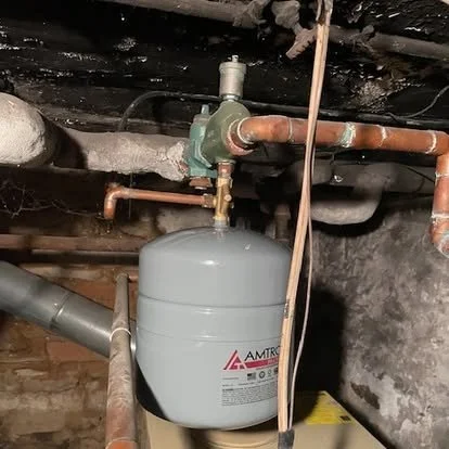 Underground water pressure tank connected to pipes and a pressure regulator in a basement setting.