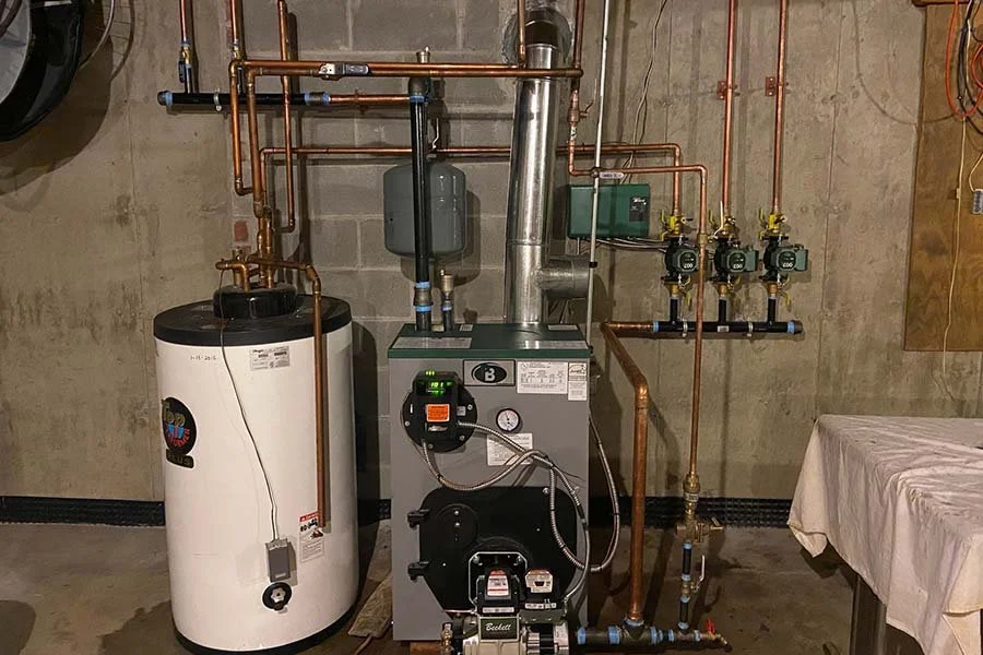 A residential heating system featuring a boiler, water heater, and network of copper pipes and gauges installed in a basement.