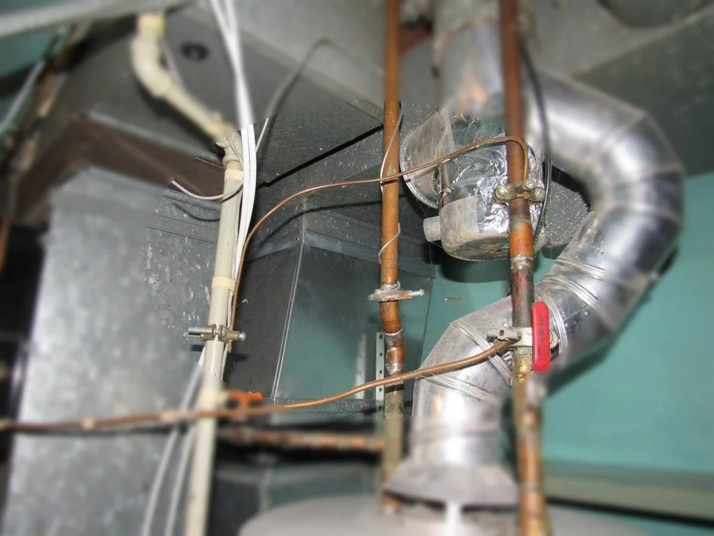 Indoor view of HVAC ductwork and pipes with metal and copper components, connected with fittings, with electrical wiring nearby.