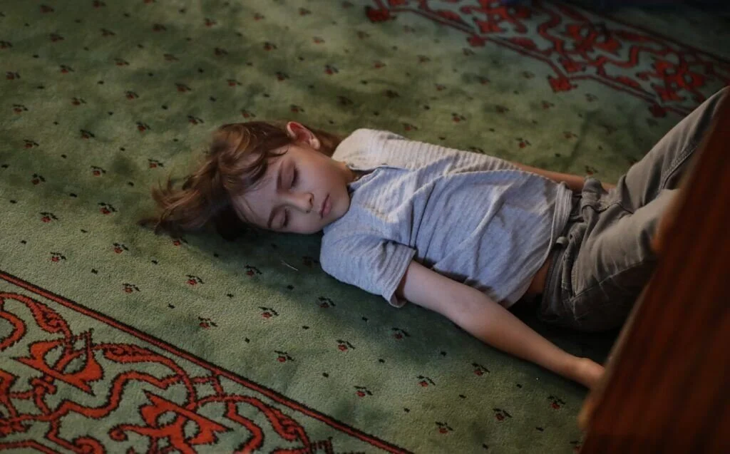 A young boy is sleeping on a green patterned carpet.