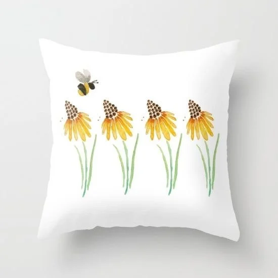 White pillow featuring a design of four yellow flowers with green stems and a bumblebee flying above them.
