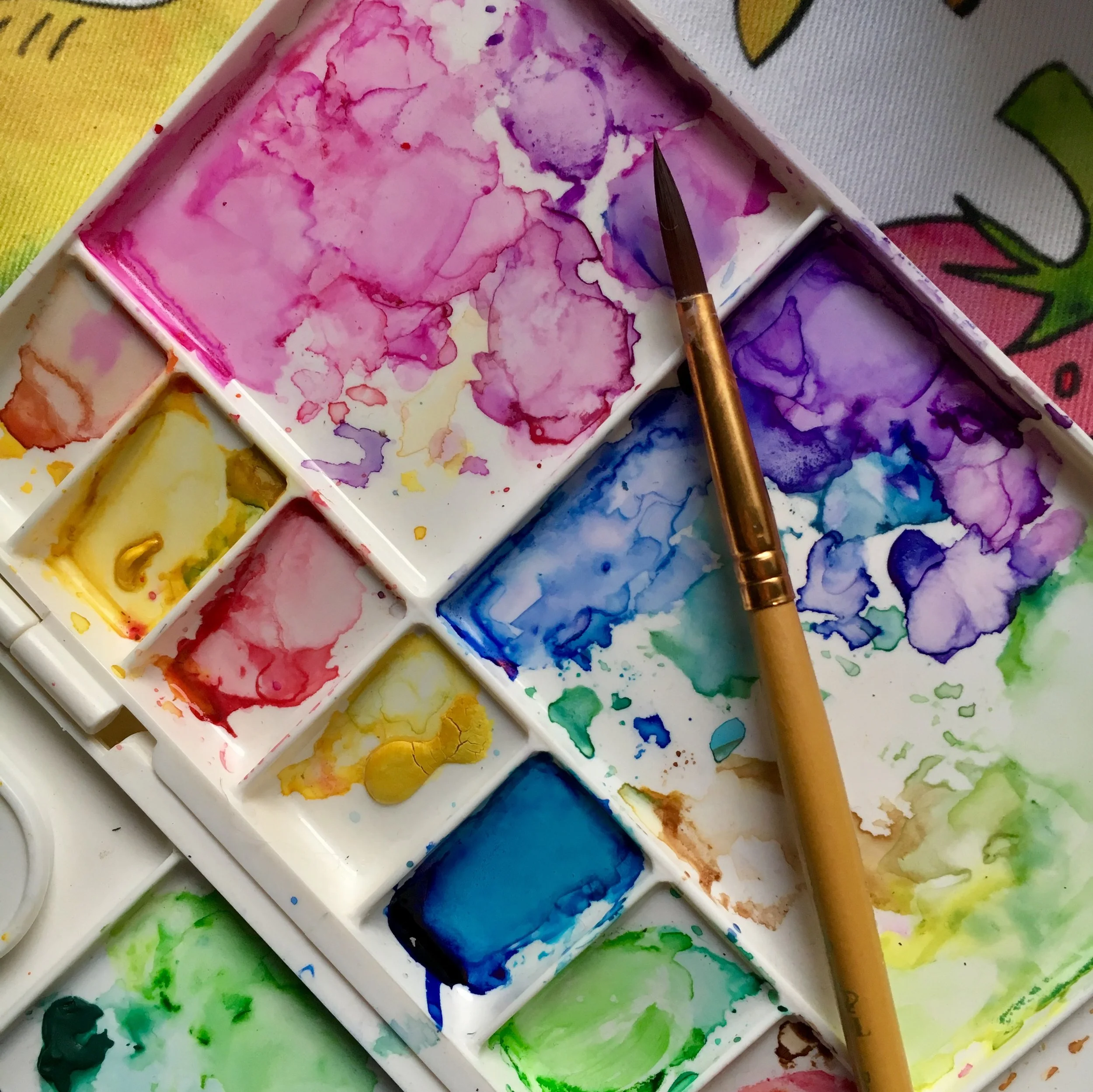 A watercolor palette with various colors and a paintbrush resting on it.