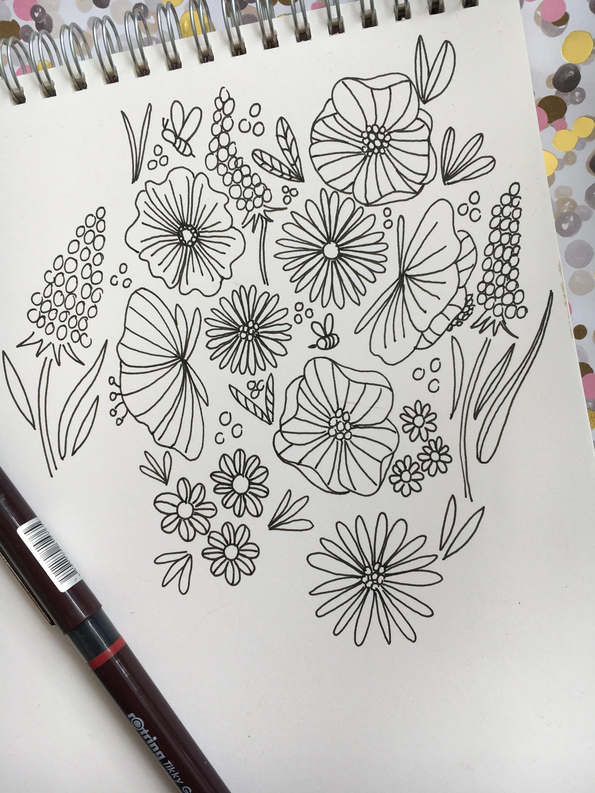 Line drawing of various flowers, leaves, and bees on a white sheet of paper, with a black pen placed on the lower left side.