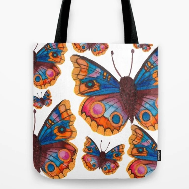 A tote bag with a colorful butterfly pattern, featuring various sizes of butterflies with blue, pink, orange, and yellow wings on a white background.