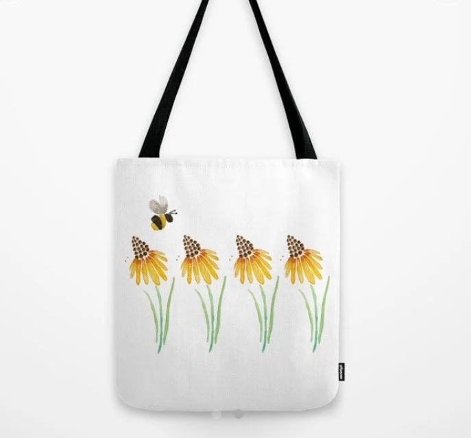 White tote bag with a design of four yellow flowers with green stems and a bee flying above.