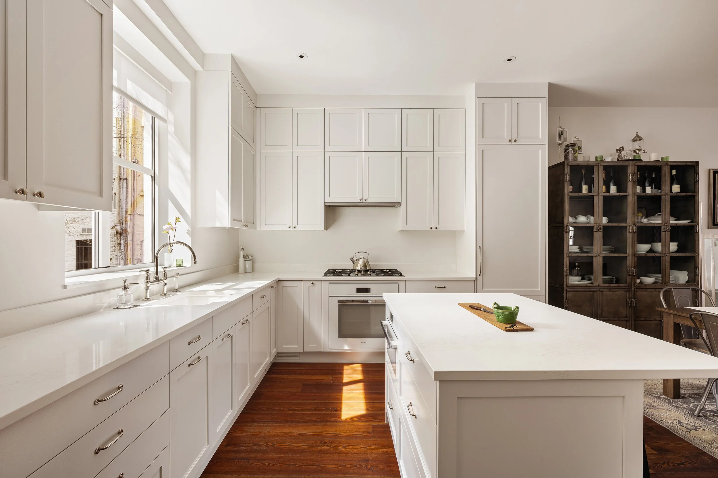 White kitchen with cabinets, a kitchen island, a window, a stove with a kettle, and wooden flooring.