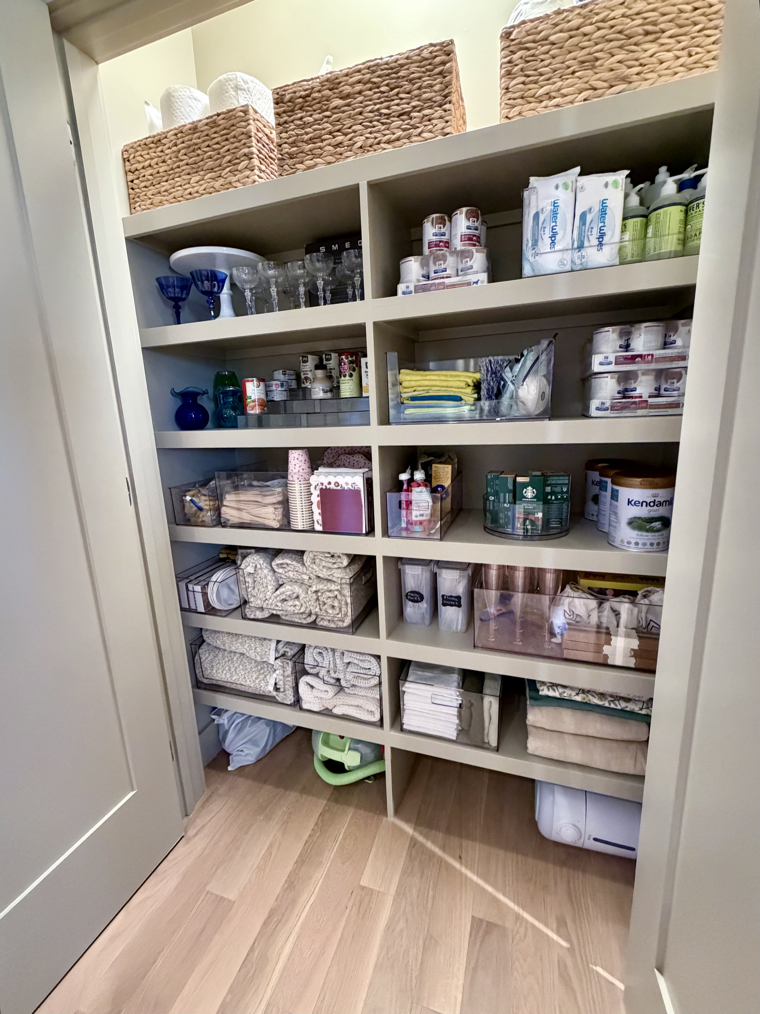 Organized multi-purpose storage closet with linens, household supplies, baby essentials and entertaining items arranged in clear bins, baskets and designated zones.