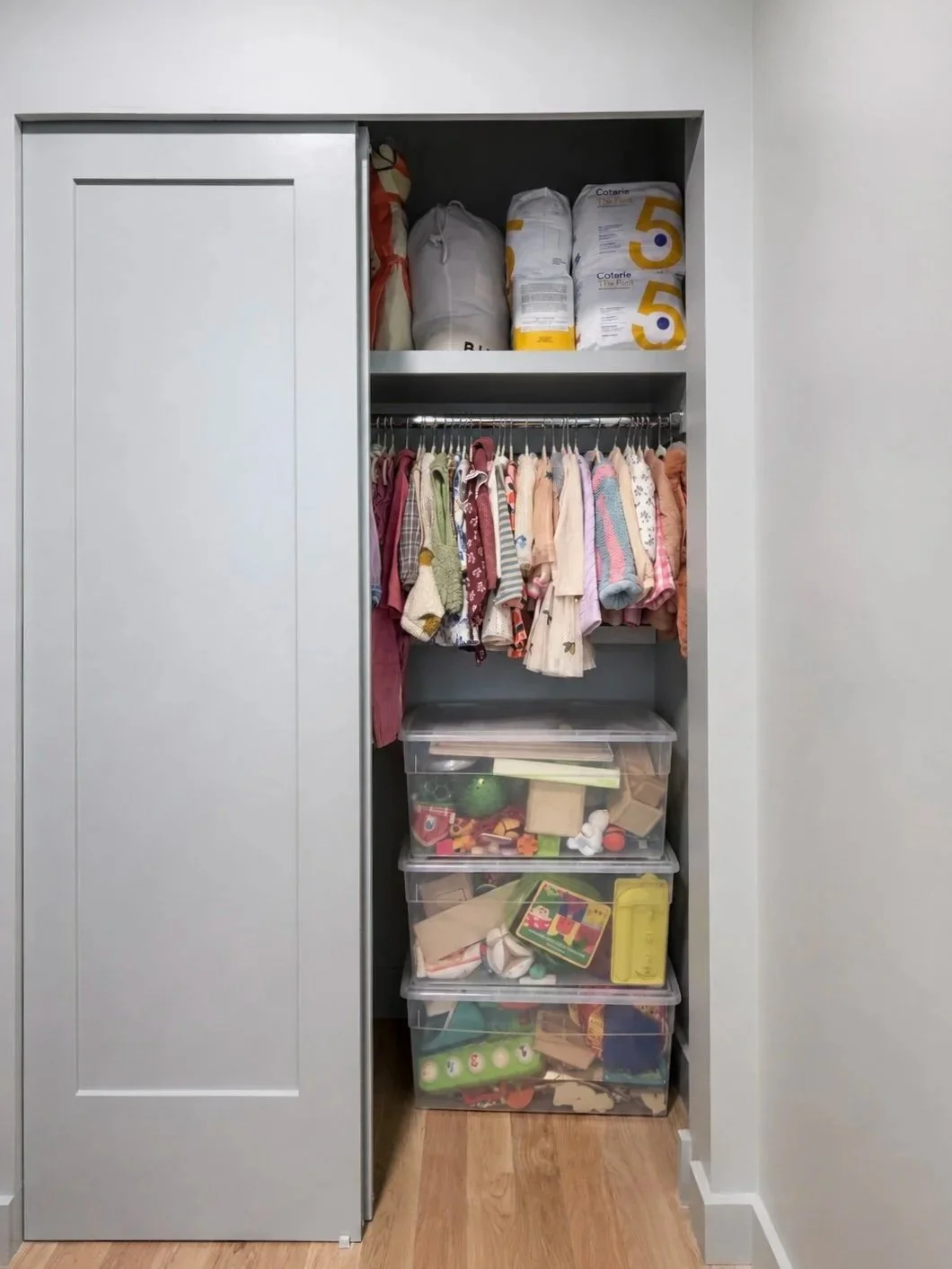 Children’s closet before organization, with hanging clothes and stacked toy storage bins.