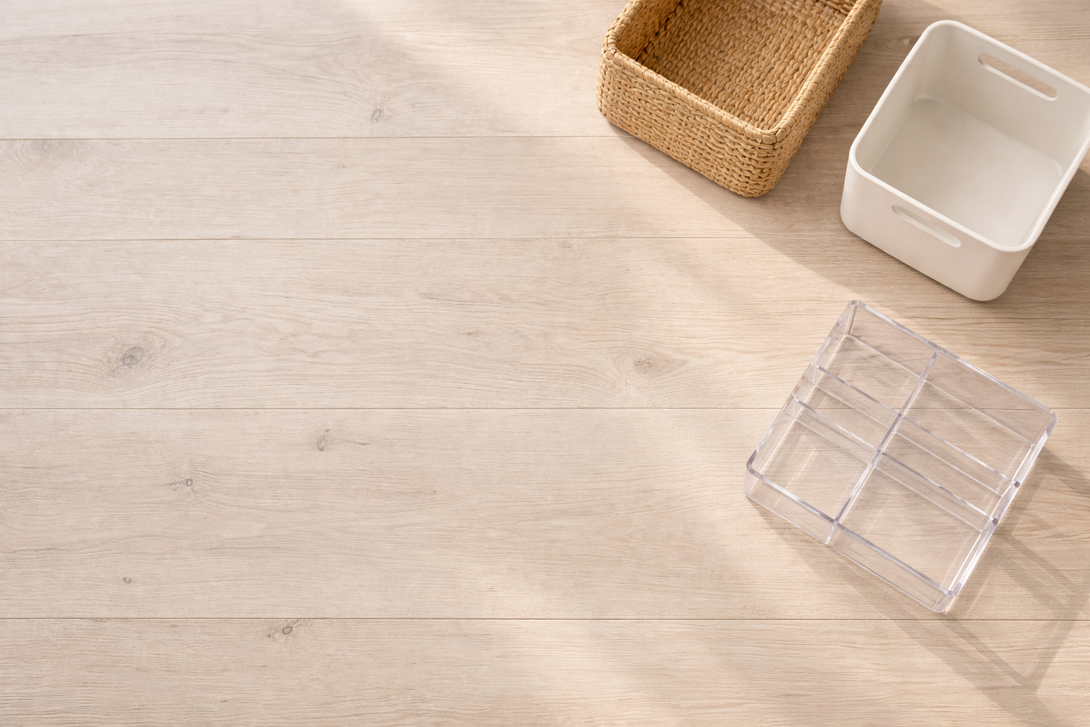 Empty wicker basket, white ceramic container, and clear acrylic organizer on a light wooden surface.