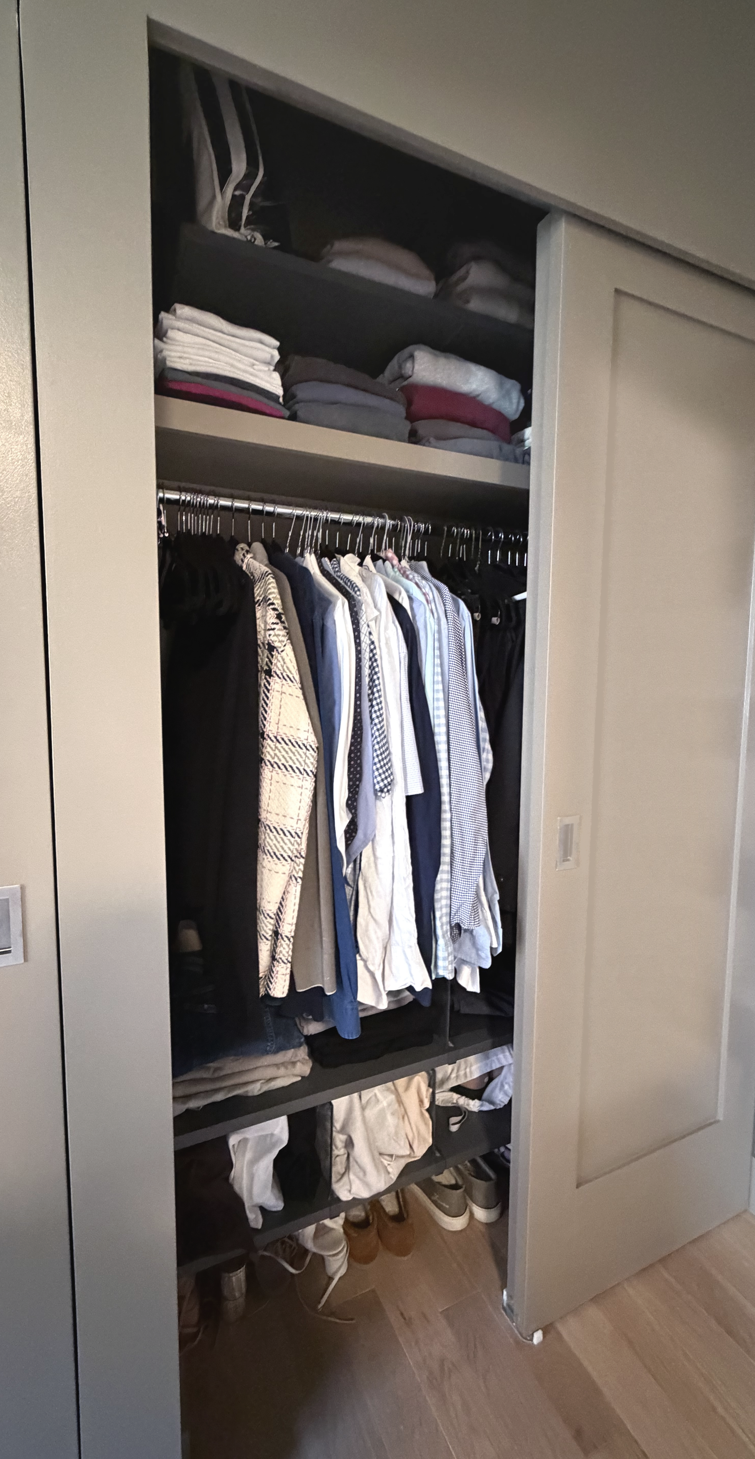 Open closet with neatly folded clothes on top shelves, hanging shirts below, and shoes on the bottom.
