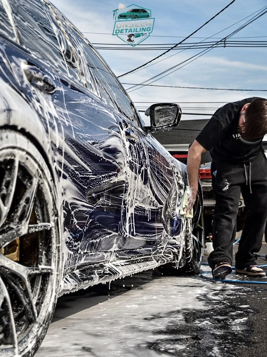 Person washing a black car with soap and water at a car wash station.