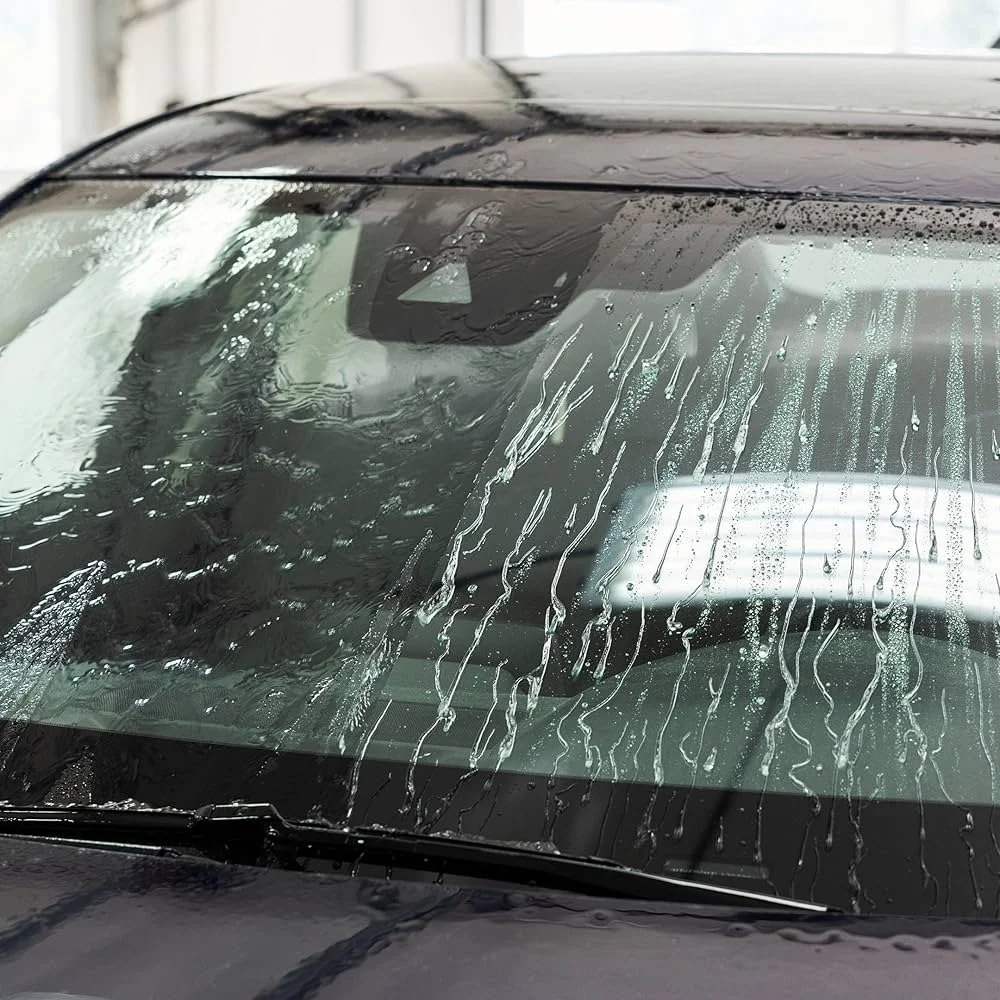 Close-up of a car windshield with water running down its surface, indicating the car is wet.