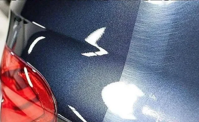 Close-up of a dark-colored car's rear with a scratched and damaged trunk surface.