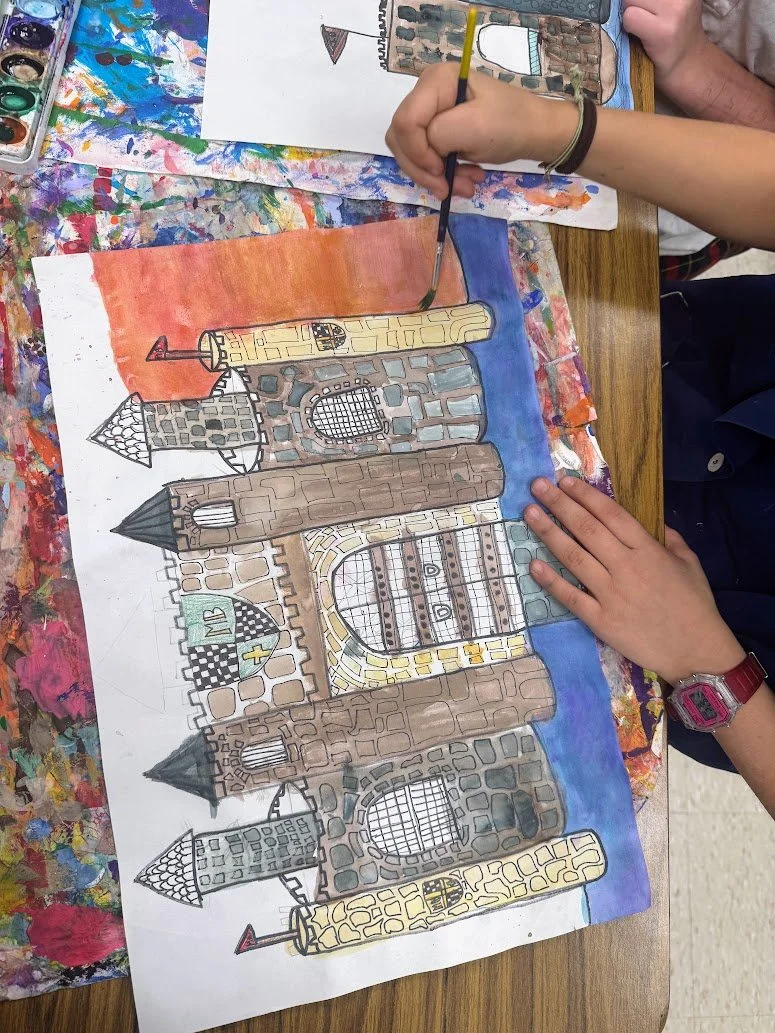 Child painting a colorful castle on paper using watercolors, with paint palette and messy table surface nearby.