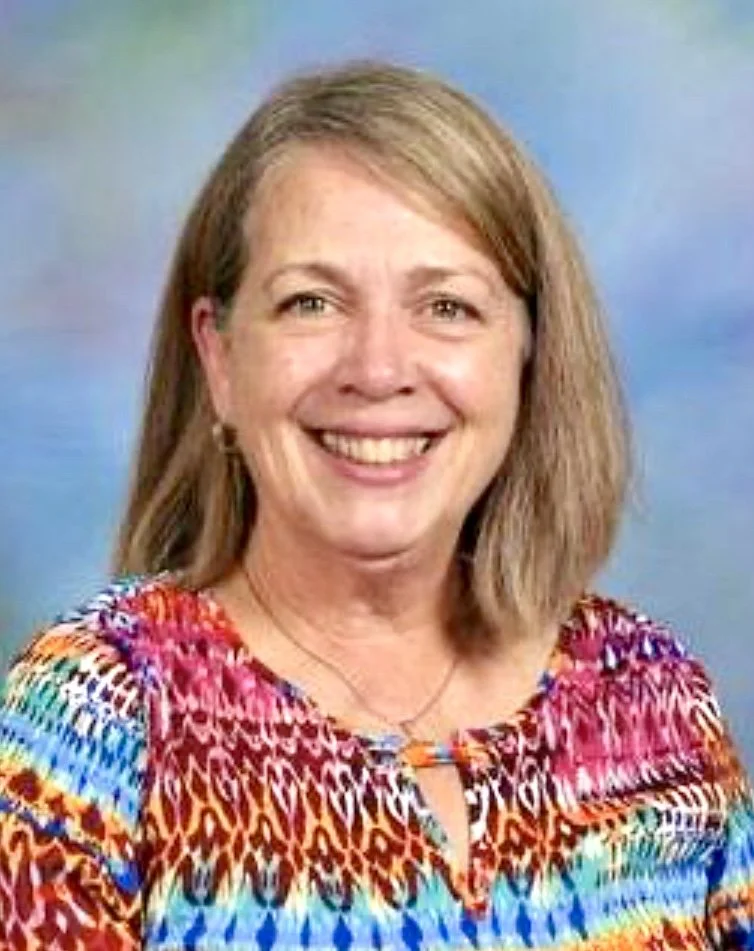 A woman smiling, wearing a colorful patterned top with a background that looks like a blue sky.