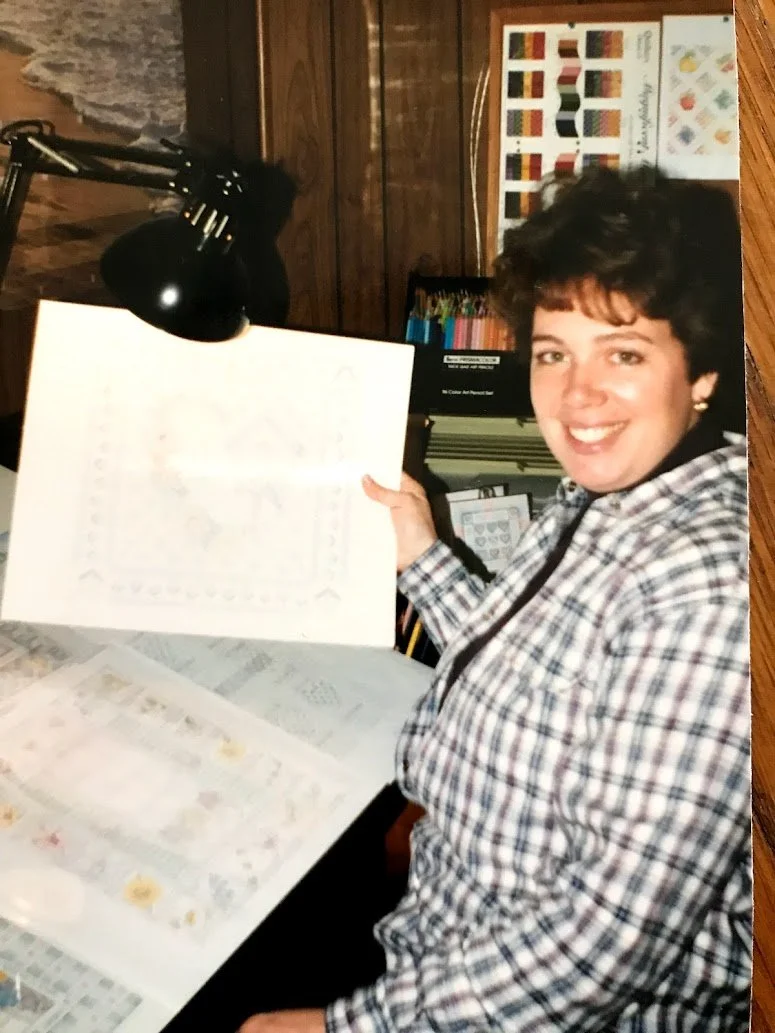 A person sitting at a desk within a cozy, wood-paneled room, smiling and holding a calendar. There are books, a lamp, and artwork on the wall behind them, creating a warm, personal workspace environment.