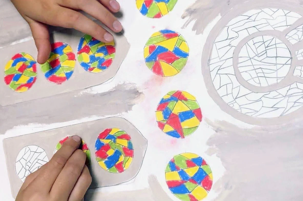 Children's hands creating colorful geometric designs on paper with circles filled with red, blue, yellow, and green shapes.