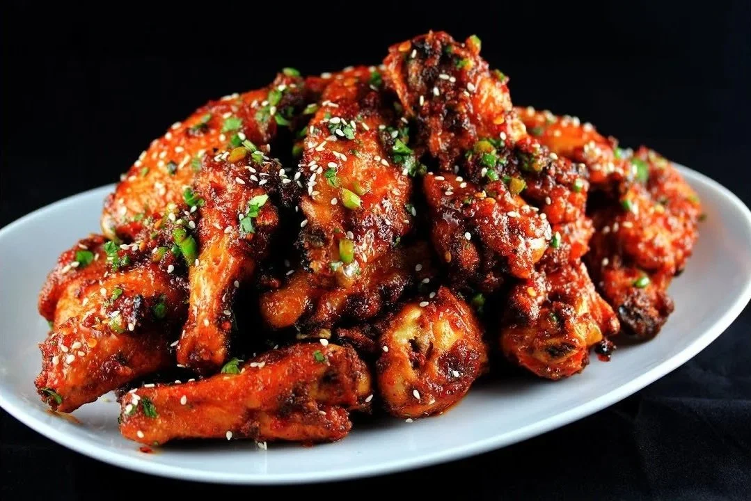 Plate of spicy buffalo chicken wings garnished with chopped green onions and sesame seeds on a white dish against a black background.