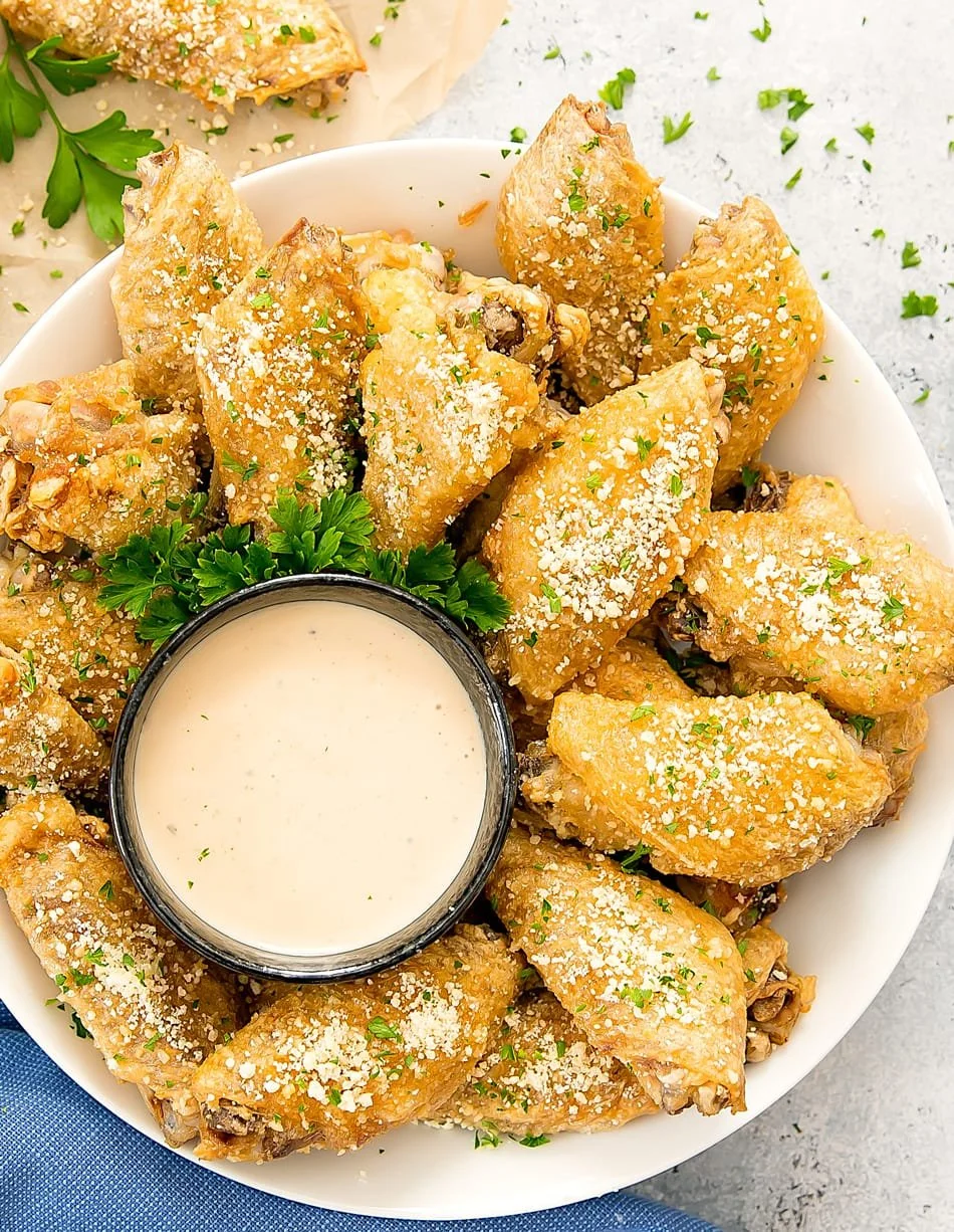 Breaded chicken wings garnished with parsley and grated Parmesan cheese, served with a side of creamy dipping sauce.