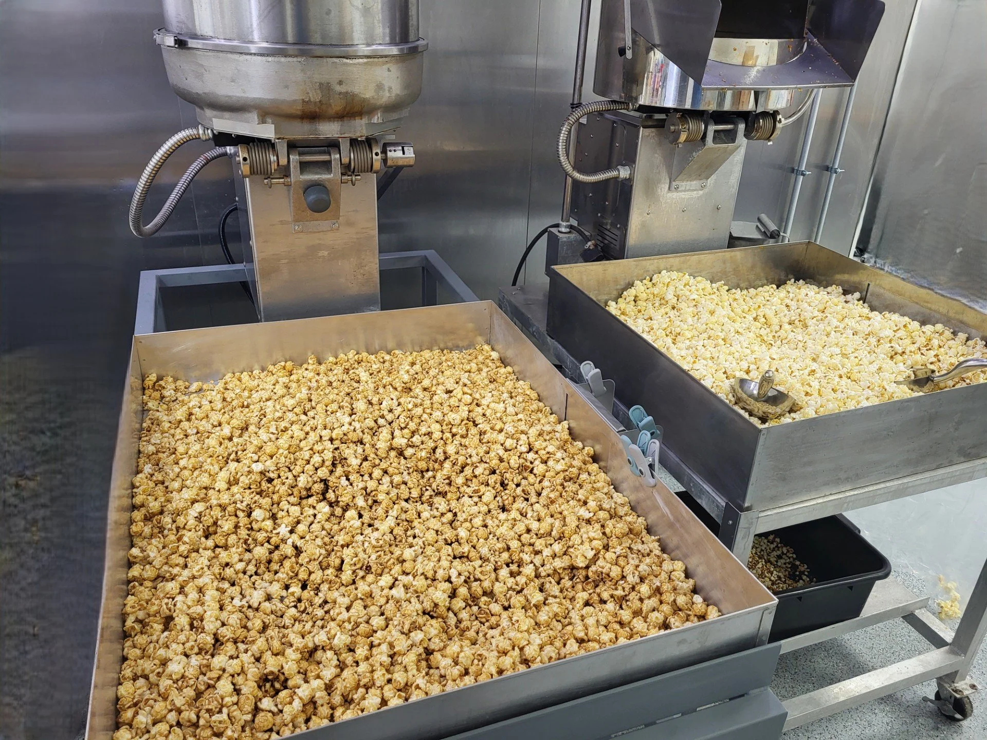 Two large metal trays filled with popcorn, one with caramel popcorn and the other with salted popcorn, in a commercial kitchen.