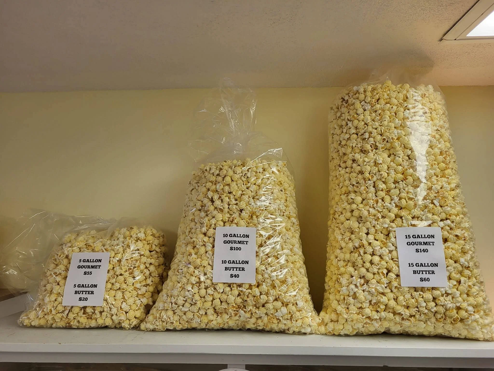 Multiple bags of gourmet popcorn labeled with different sizes and prices, including 5-gallon, 10-gallon, and 15-gallon options.