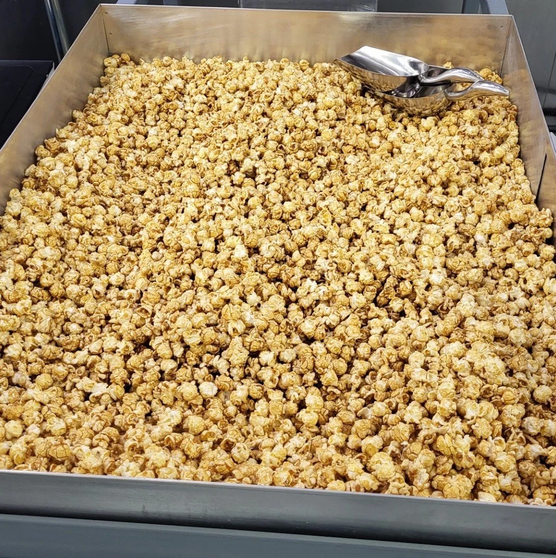 A large tray filled with caramel popcorn and metal scoops.