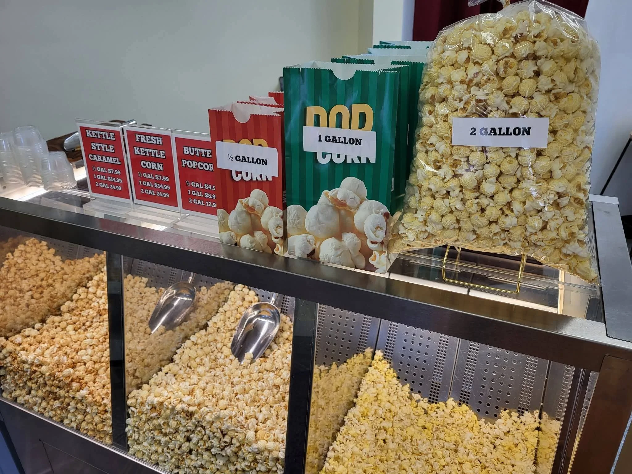 Display of popcorn in a retail or concession stand with signs indicating quantities and prices, with different bags of popcorn in various sizes.