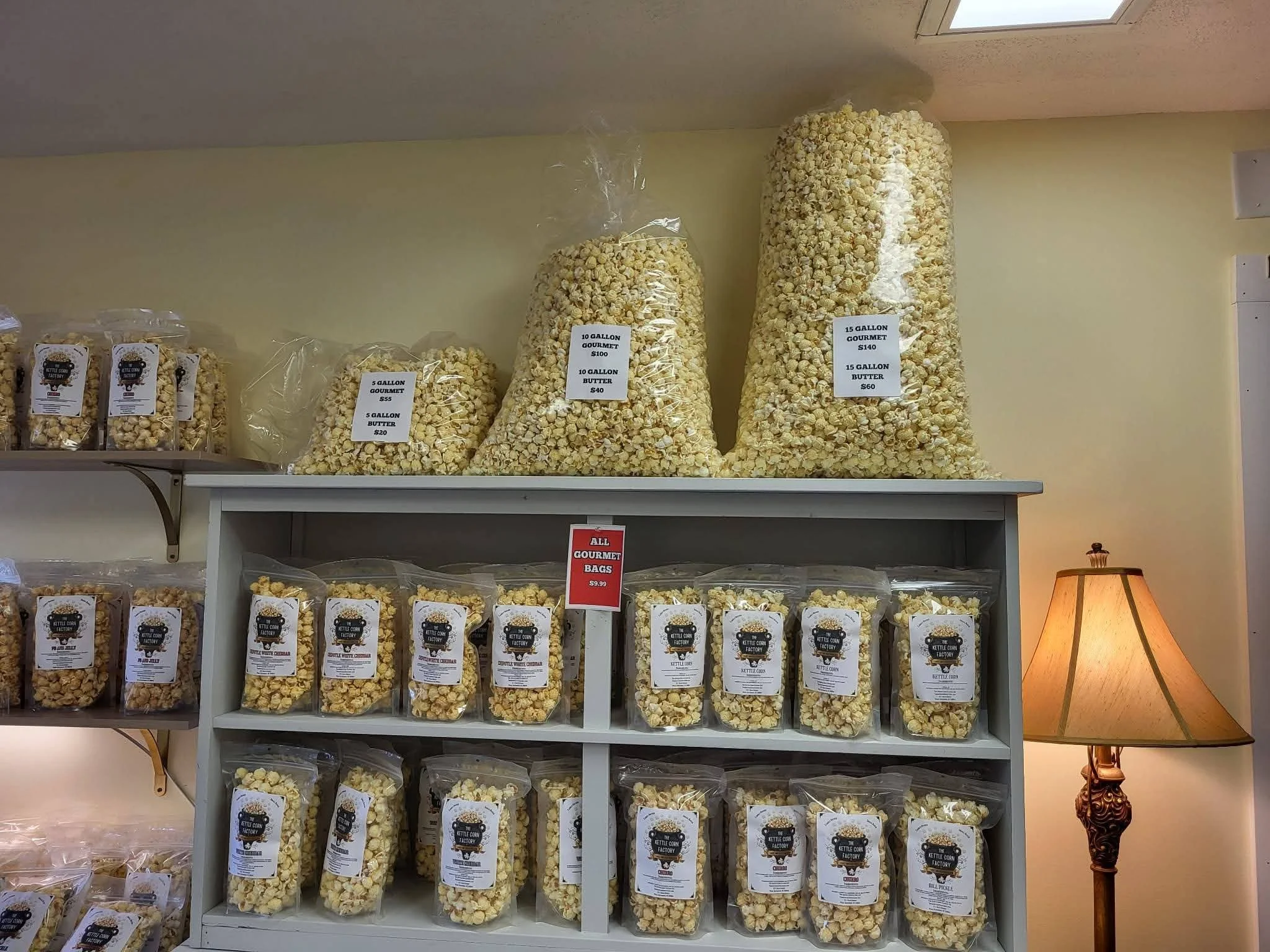 Multiple large and small bags of popcorn and popcorn products displayed on shelves in a store, with price tags specifying sizes and costs.