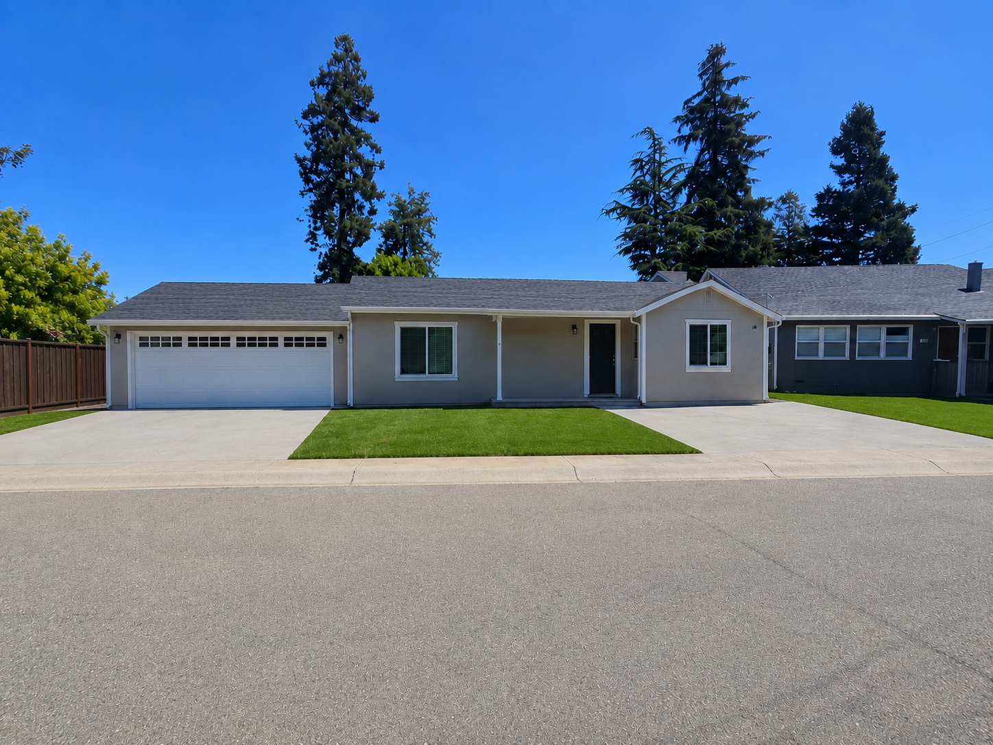 Front view of a modern, detached single-story house with a two-car garage, a small front lawn, driveway, and clear blue sky.