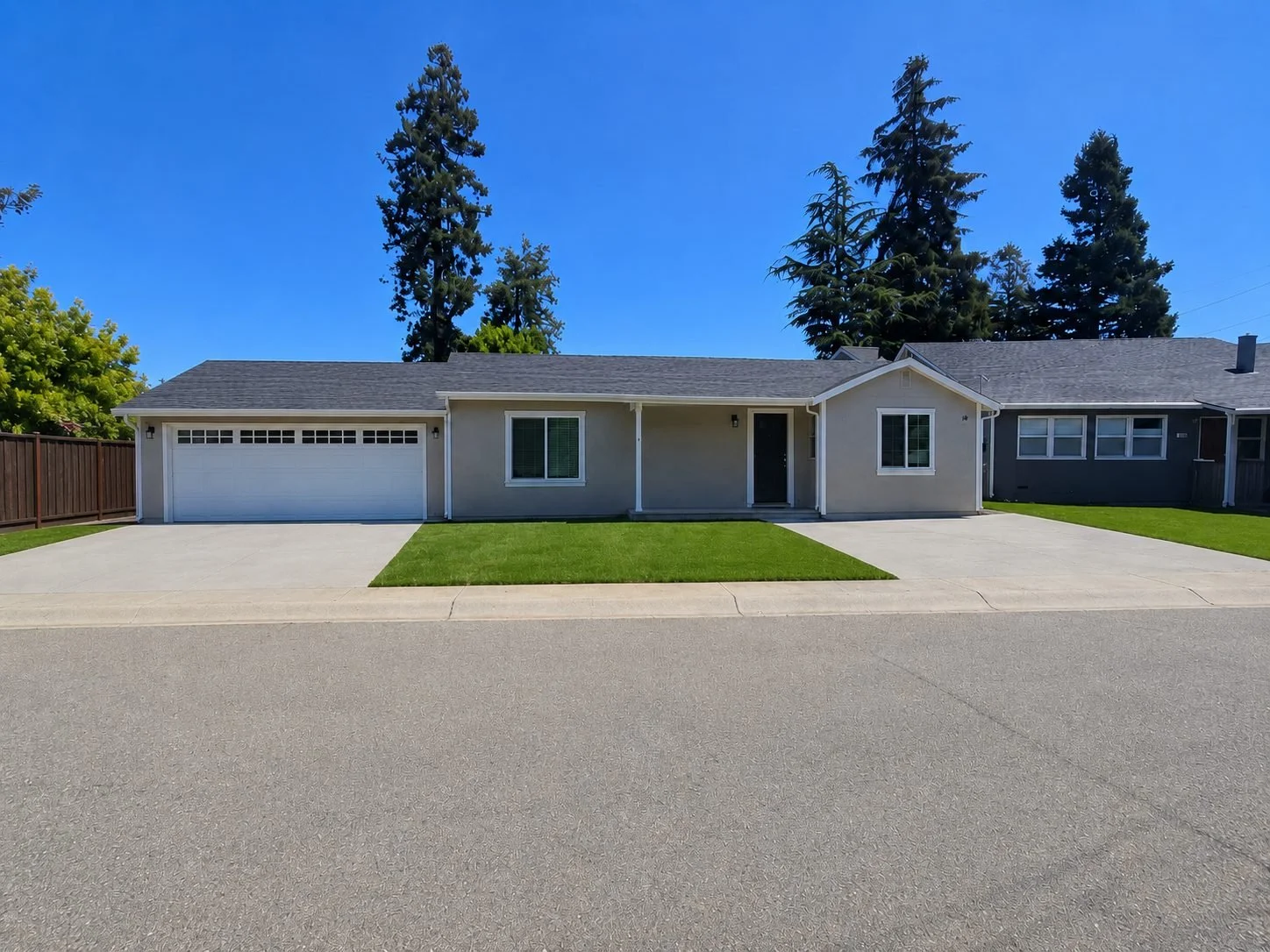 Front view of a modern, detached single-story house with a two-car garage, a small front lawn, driveway, and clear blue sky.