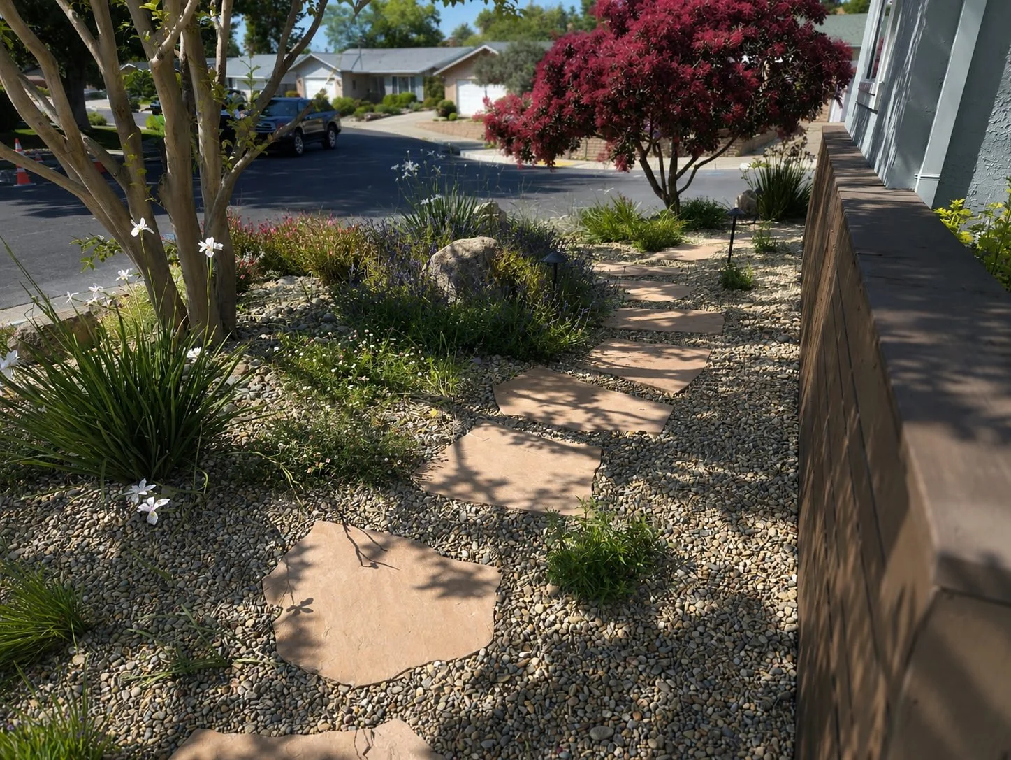A landscaped front yard with a stone pathway, various plants, and trees, beside a wooden fence and residential street.