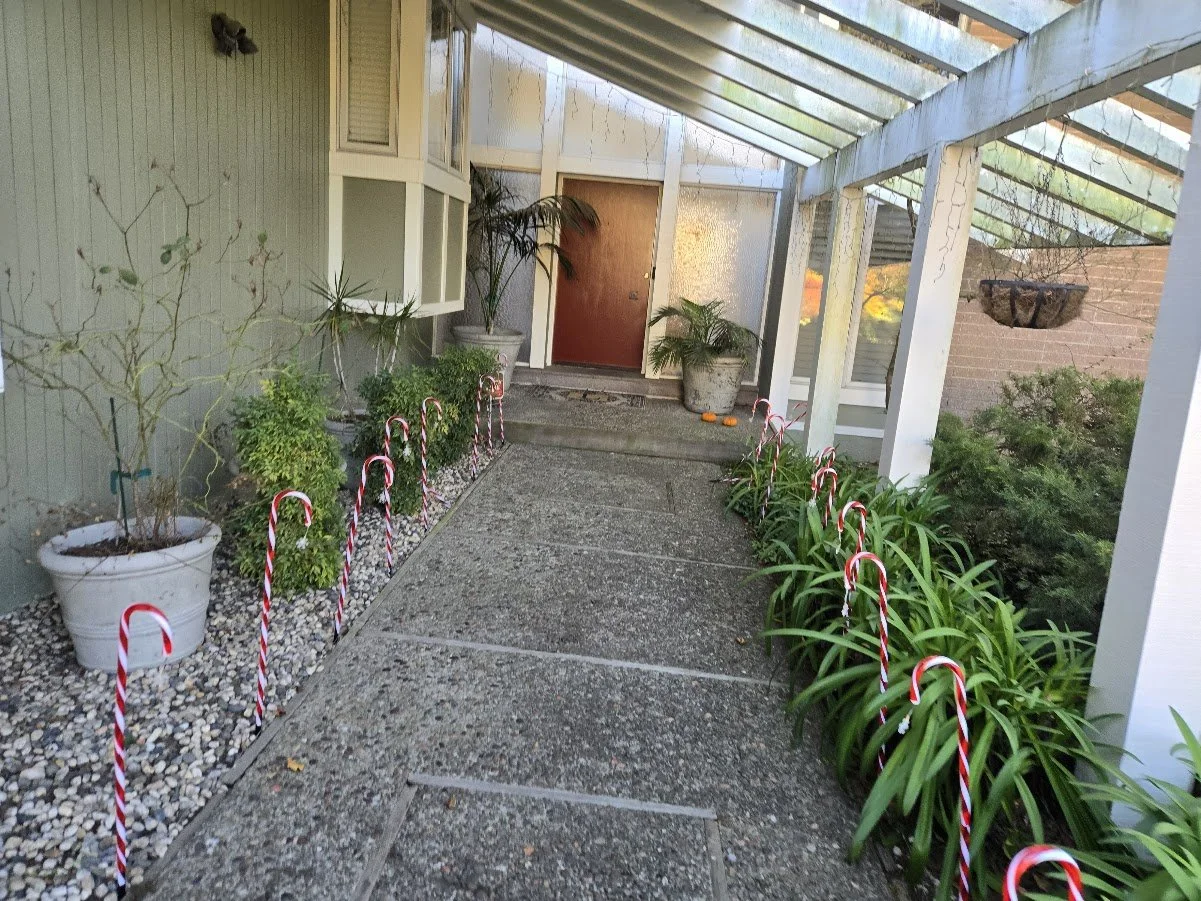 Front porch with potted plants, candy cane decorations along walkway, and a brick door with a glass overhang.