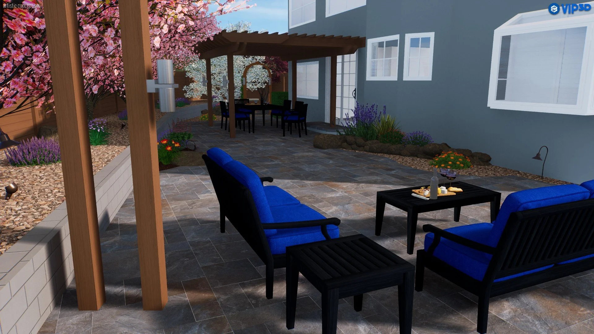 A landscaped backyard patio with blue cushioned chairs, a black table with snacks and wine, a wooden pergola, flowering trees, and garden beds with purple, white, and orange flowers next to a house with gray walls and white windows.