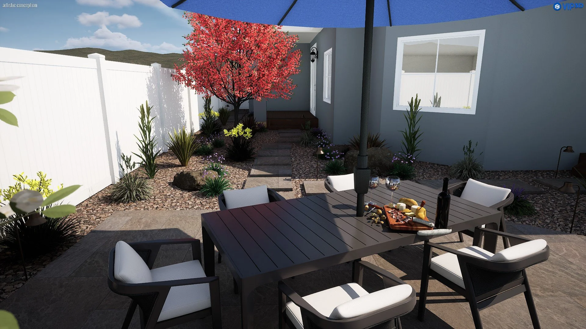 A backyard patio with a dining table set up under an umbrella, surrounded by outdoor chairs. There's a gravel garden with a pink-flowered tree, small plants, and rocks. The house has a gray exterior with windows, and there are mountains and a blue sk
