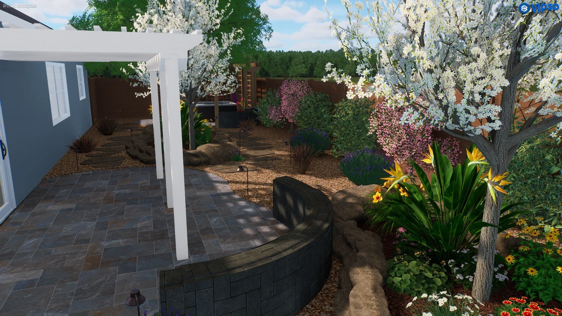 A backyard garden with a paved patio in the foreground, surrounded by a variety of colorful flowering plants, shrubs, and trees, including white, pink, and yellow blossoms. A white pergola is partially visible on the left, and there is a wooden fence