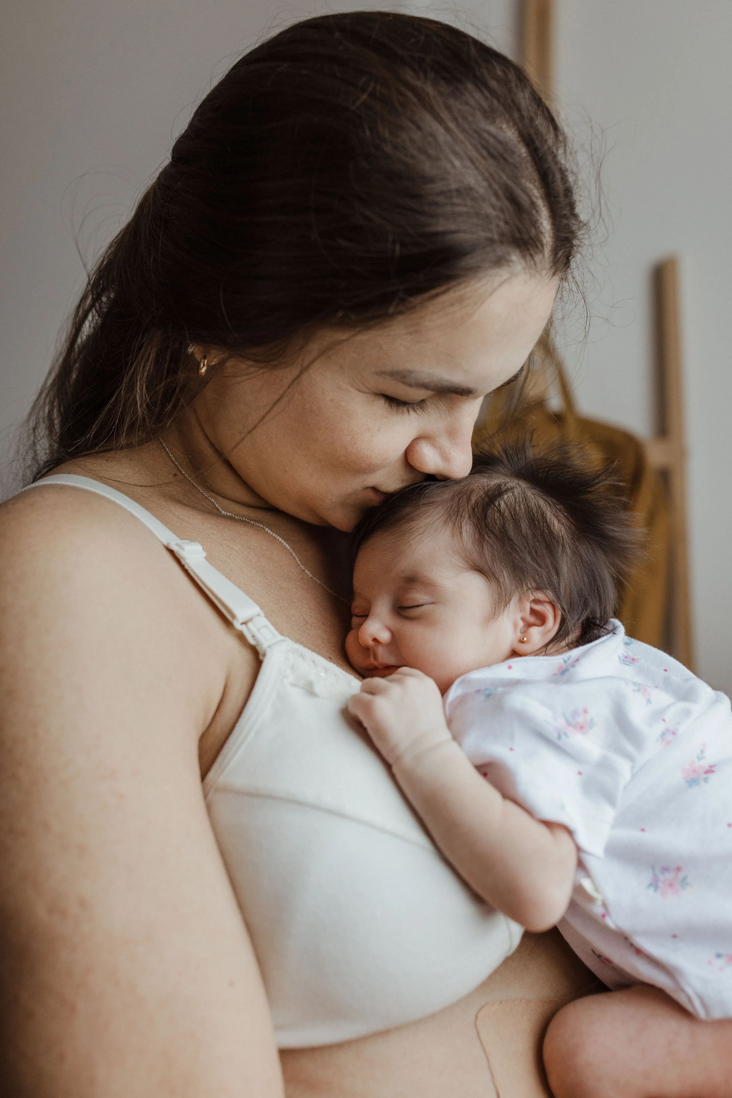 A mother holding her sleeping newborn, supported through postpartum recovery by The Mothers Village postpartum team.