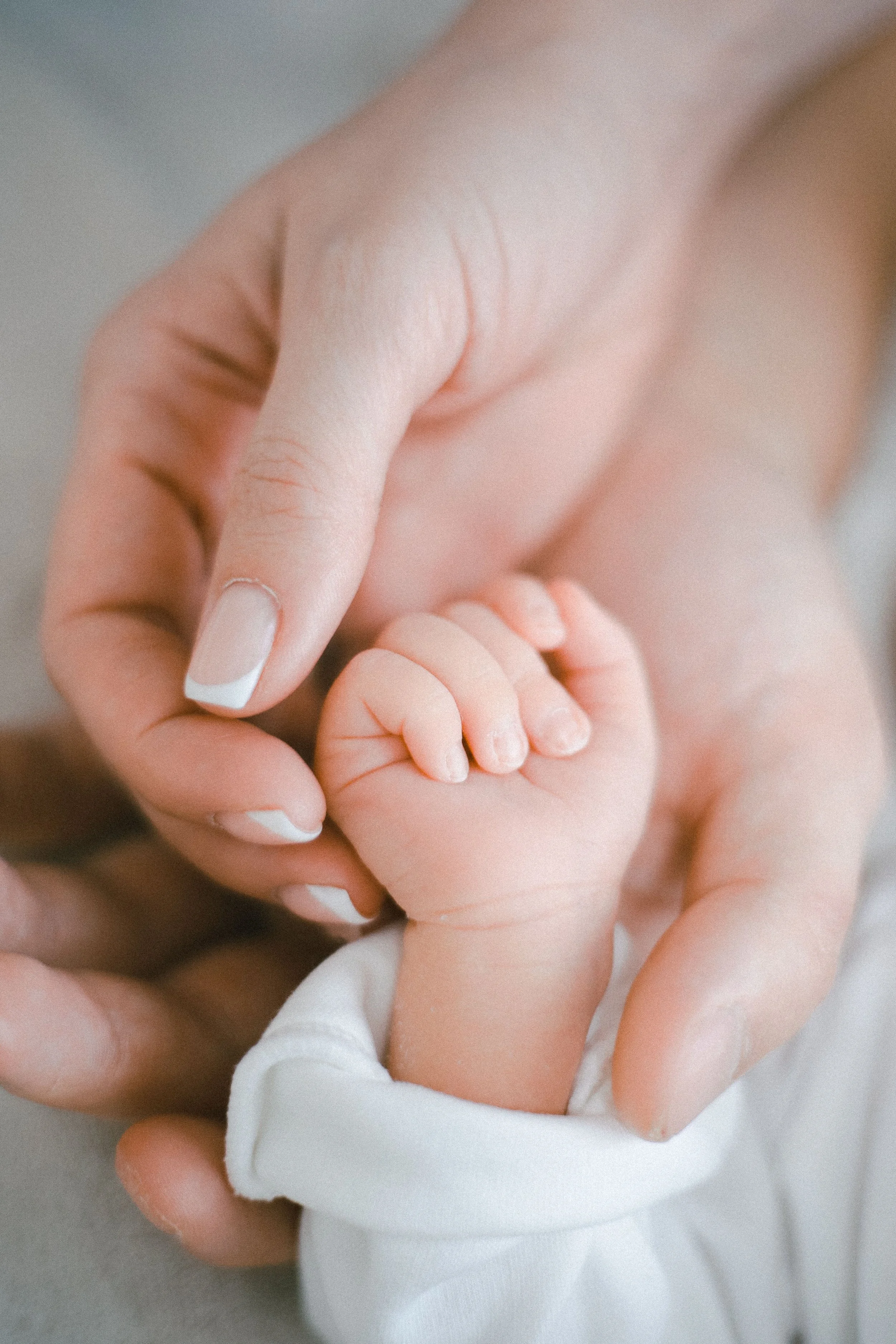 Close-up of a baby holding an adult's finger with an adult hand also visible.