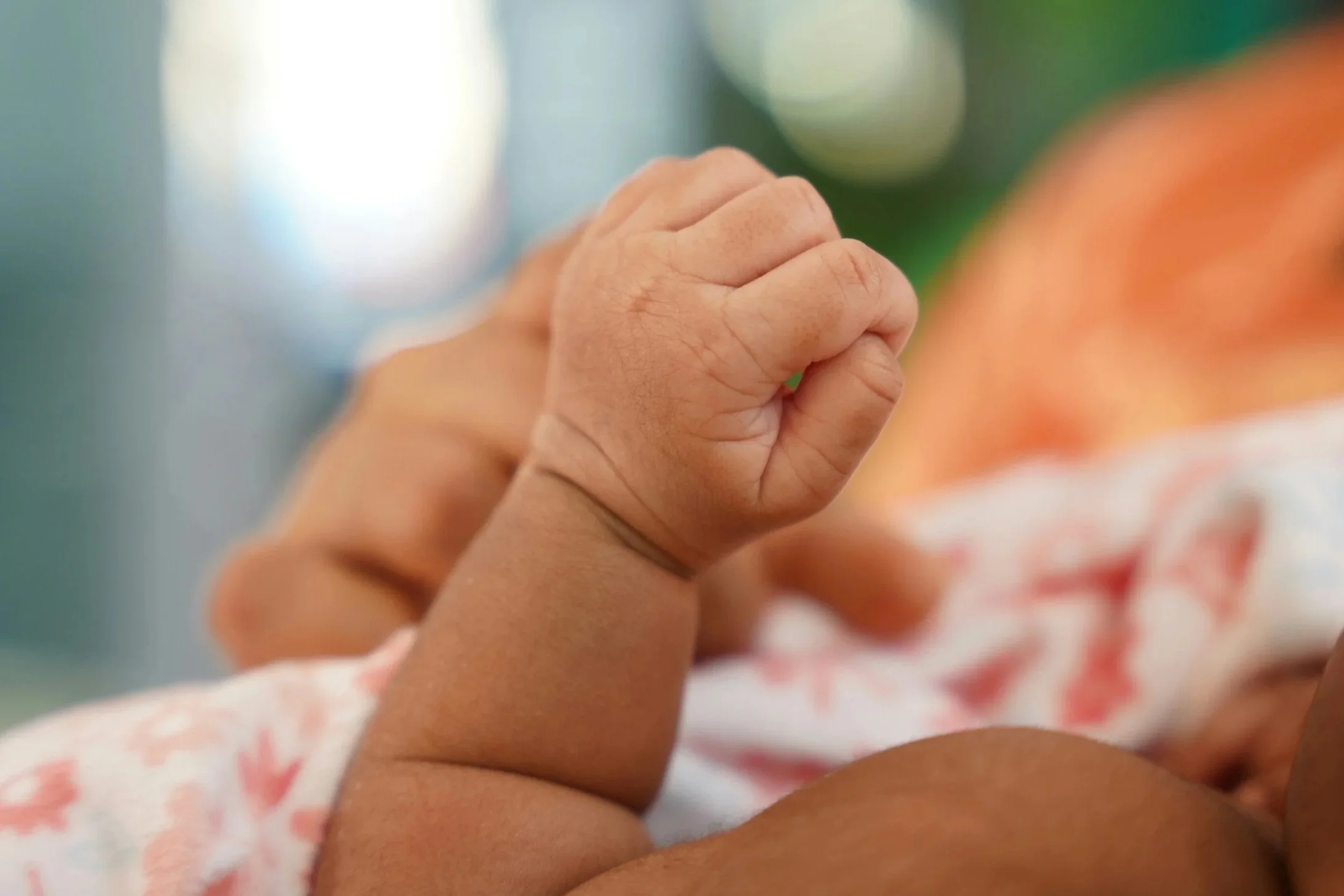 Close-up of a baby with hands clasped together, with soft focus on background.