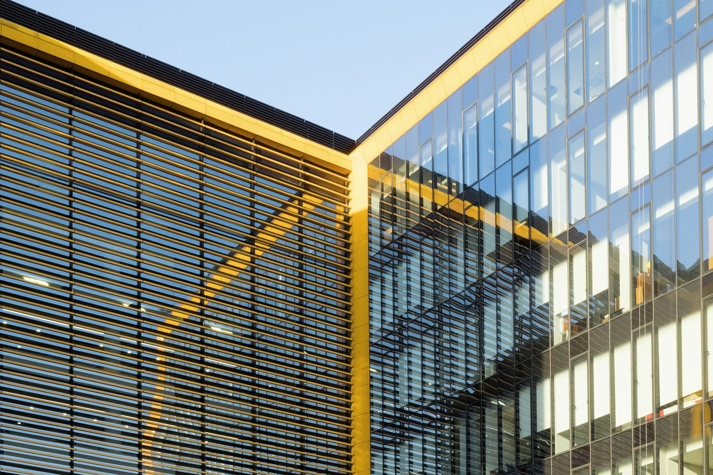 Close-up of modern glass office building with reflective windows and yellow and black horizontal decorative elements under a clear blue sky.