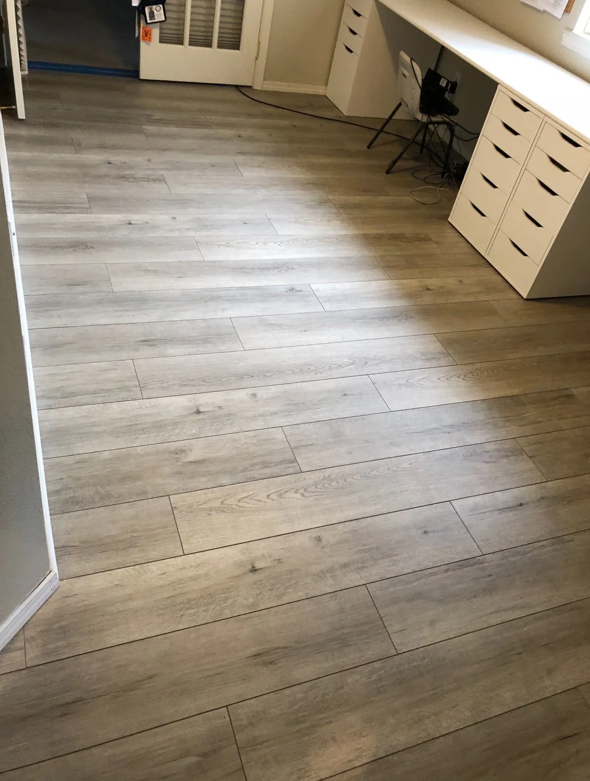 Light-colored wood flooring in an office or workroom area with white cabinetry and a desk with wiring and electronic equipment.