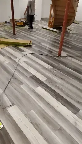 Construction worker installing laminate flooring in a room with a staircase.