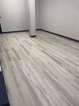 Empty room with white walls, a pillar, and light wooden flooring.