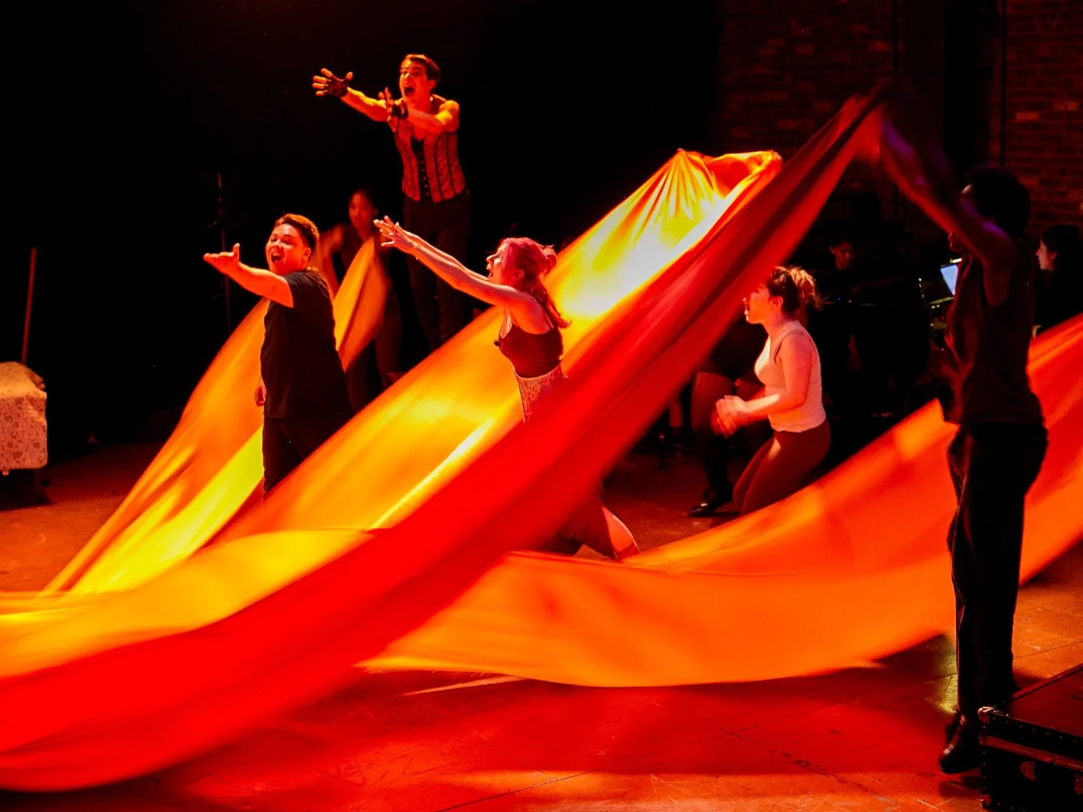Performer on stage with a large, flowing orange fabric, engaging with the audience during a theatrical performance.