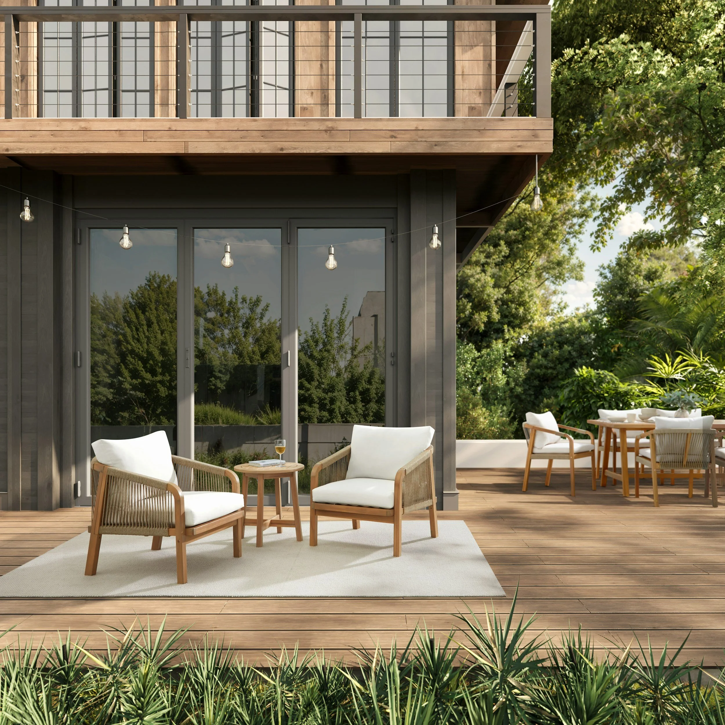 Outdoor patio area with modern furniture, a wooden deck, string lights, and lush green trees in the background.