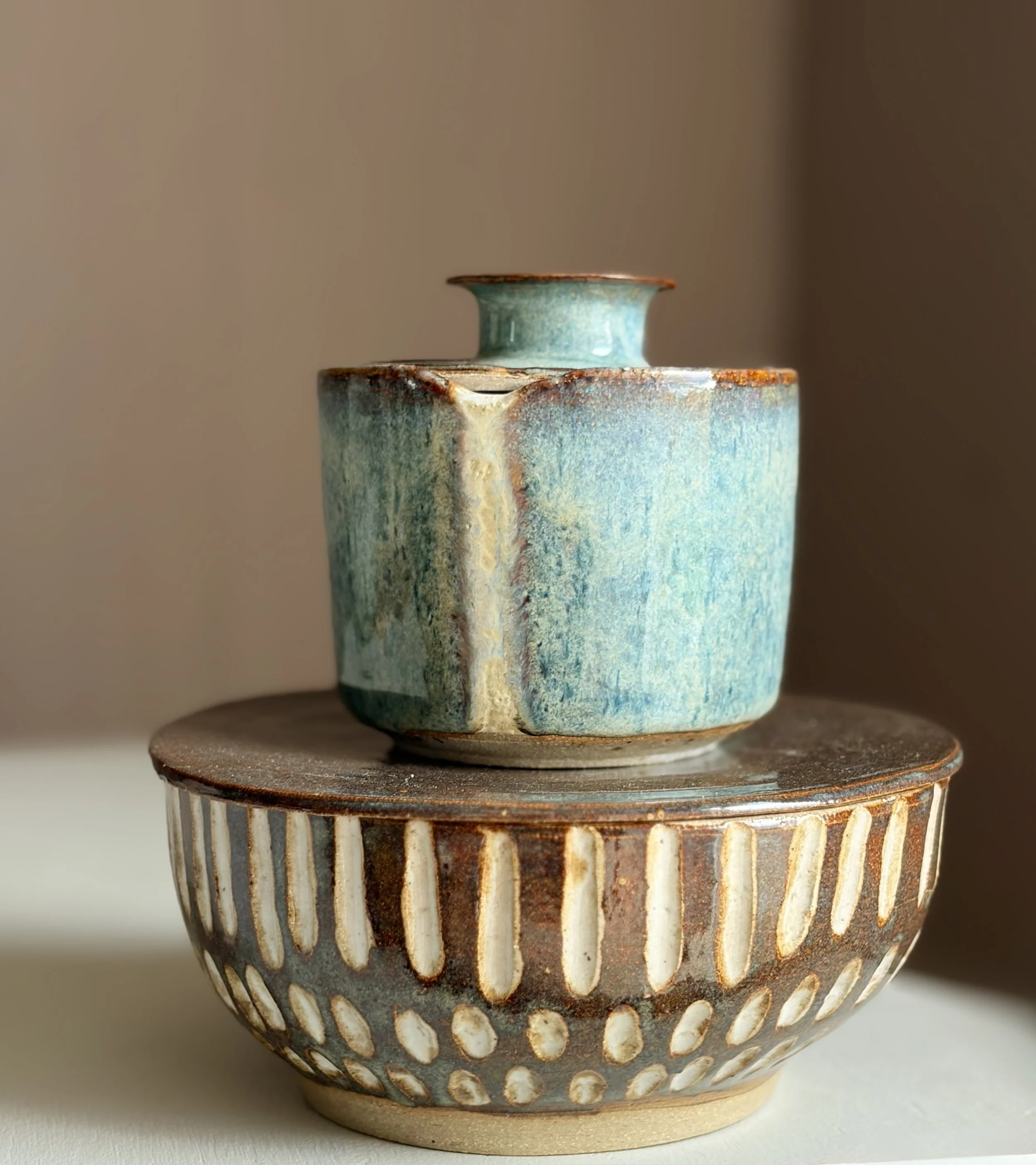 Close-up of a ceramic vase with a turquoise glaze, featuring vertical, white, elongated oval cutouts around its body, placed on a wooden surface.