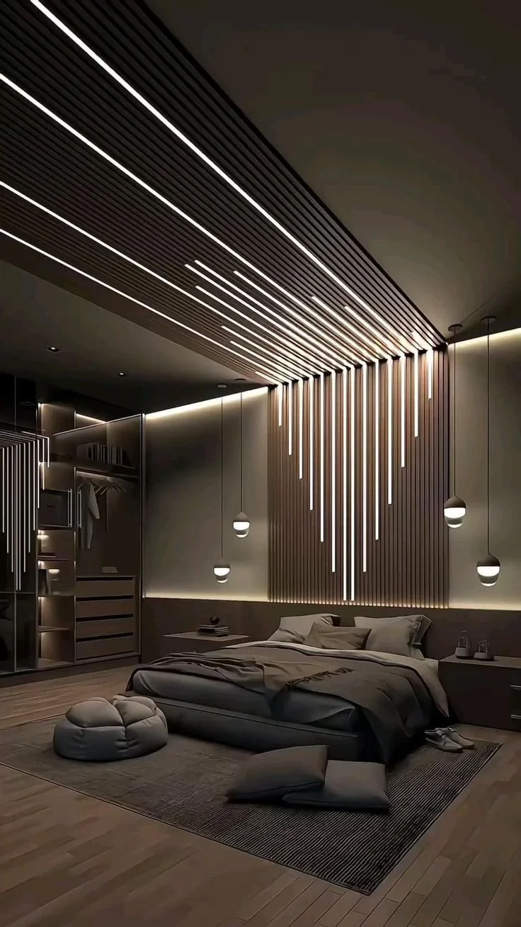 Modern bedroom with minimalist design, illuminated by decorative pendant and strip lighting, featuring a bed with disheveled bedding, seating cushions on the floor, and built-in closet shelves.