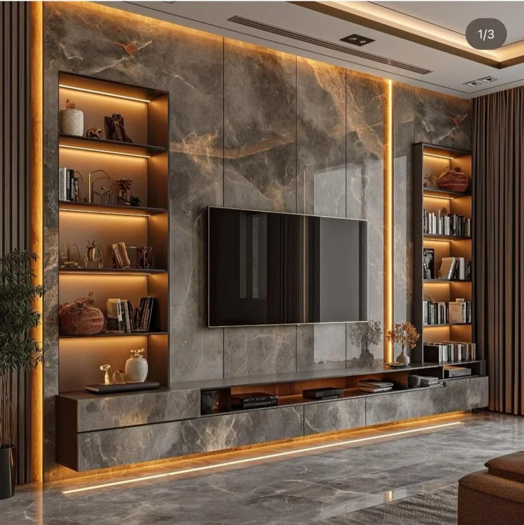 Modern living room wall with a mounted flat-screen TV, gray marble panels with gold lighting accents, two built-in bookshelves with LED lighting, and a low marble console. Decorative items and books are on the shelves.